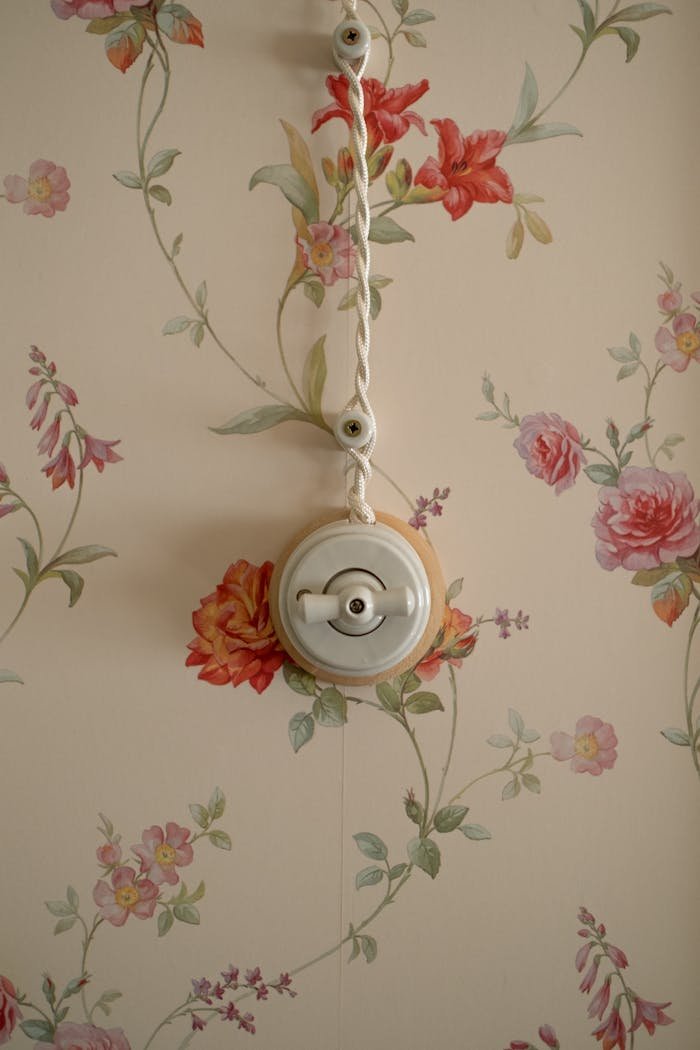 A vintage style light switch mounted on elegant floral pattern wallpaper.